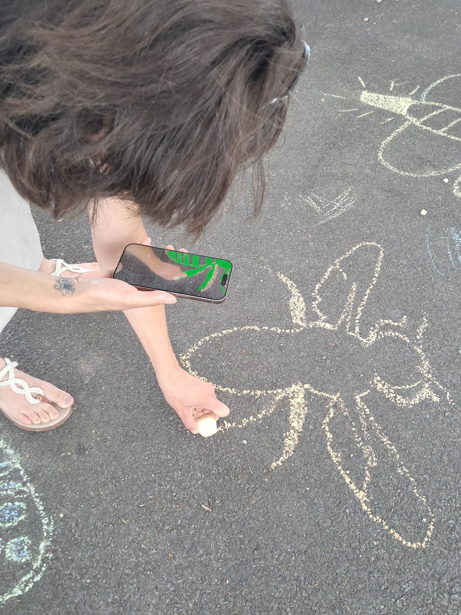 Tracing a chalk bumble bee on a driveway by following the Plancast AR overlay on a phone held in one hand